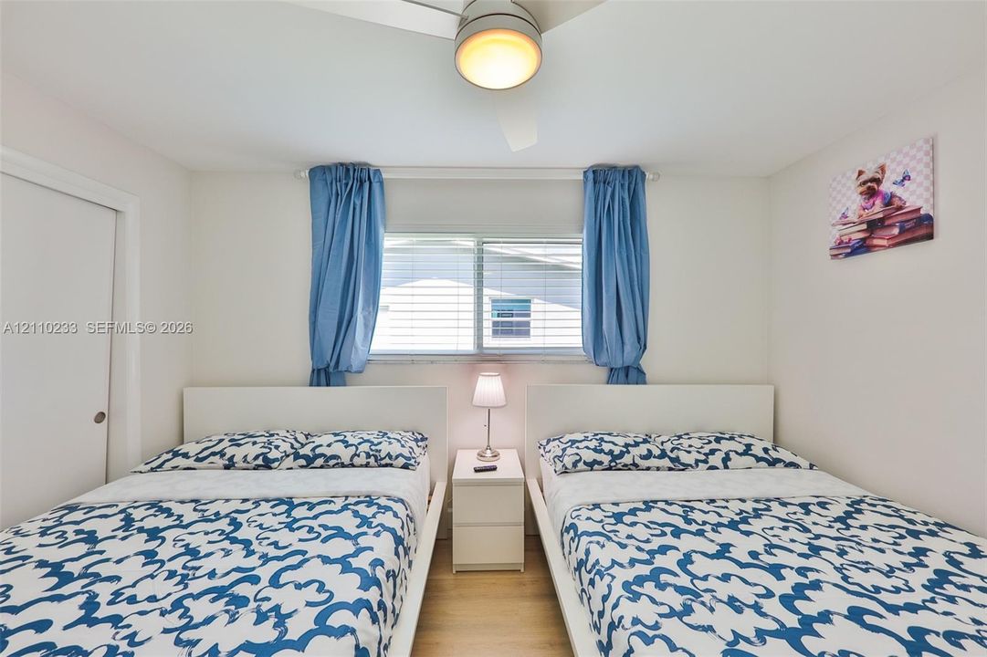 Room featuring wood-finish flooring, a central ceiling fan with integrated lighting, and a window with horizontal blinds