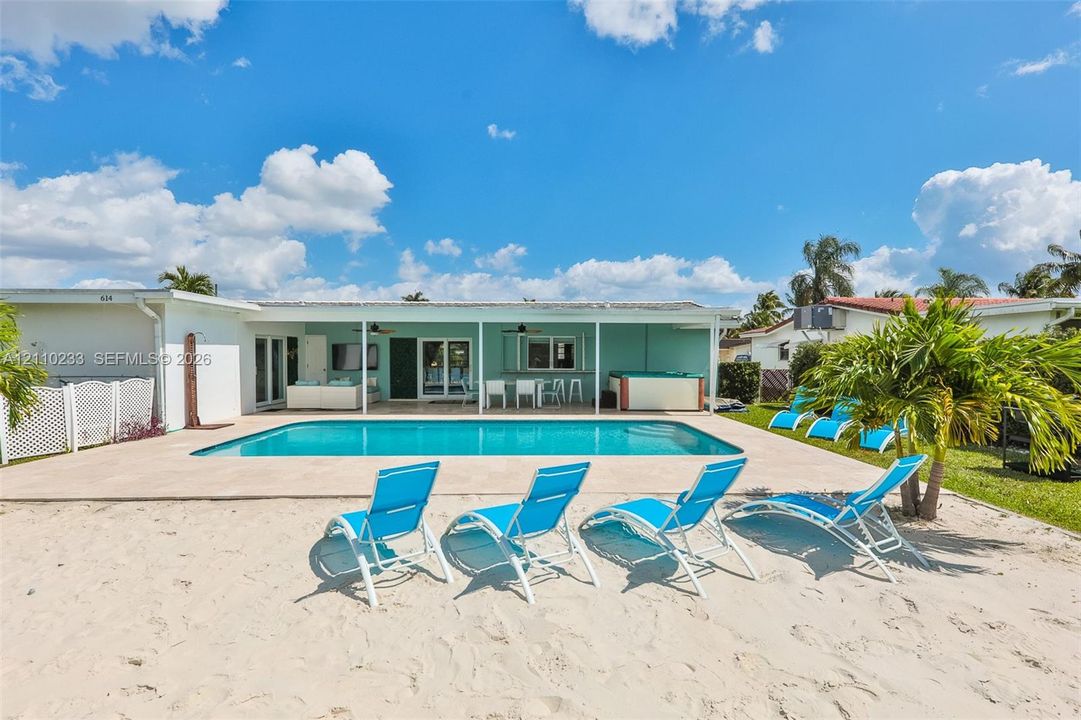 In-ground swimming pool with an expansive concrete deck, covered patio space, and a private sandy beach area