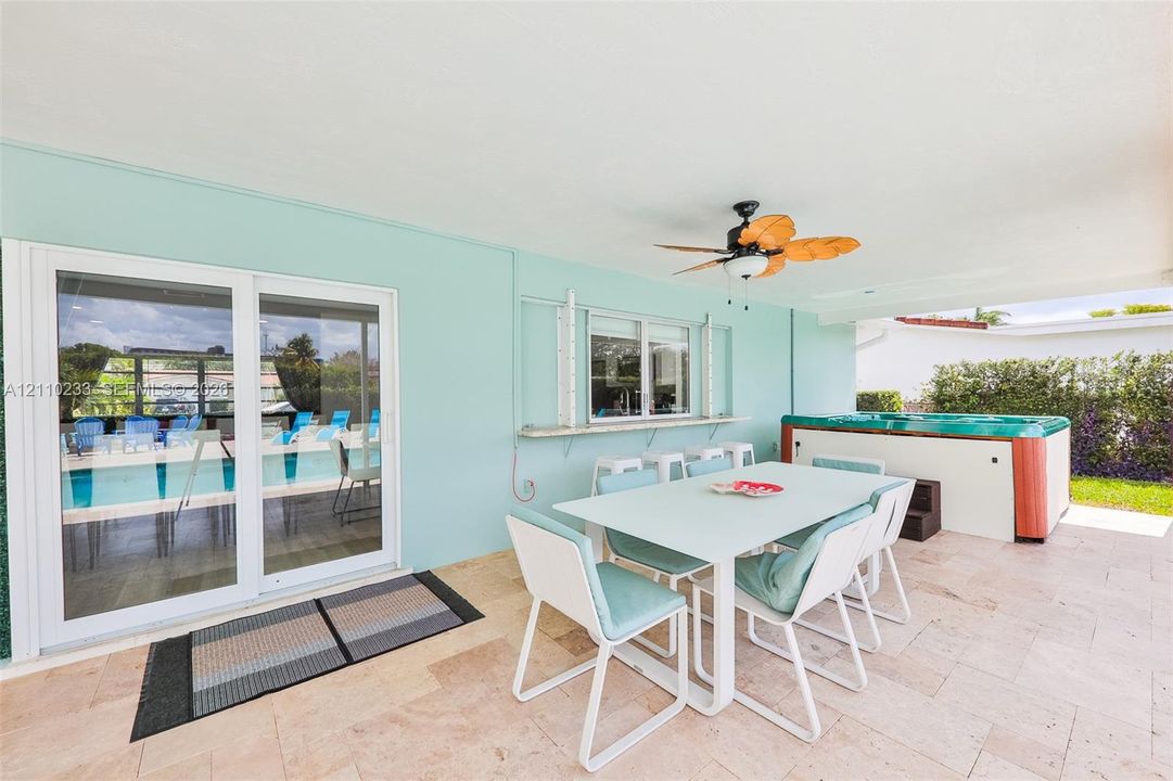 Covered patio featuring stone tile flooring, an integrated serving ledge, a ceiling fan, and a built-in spa