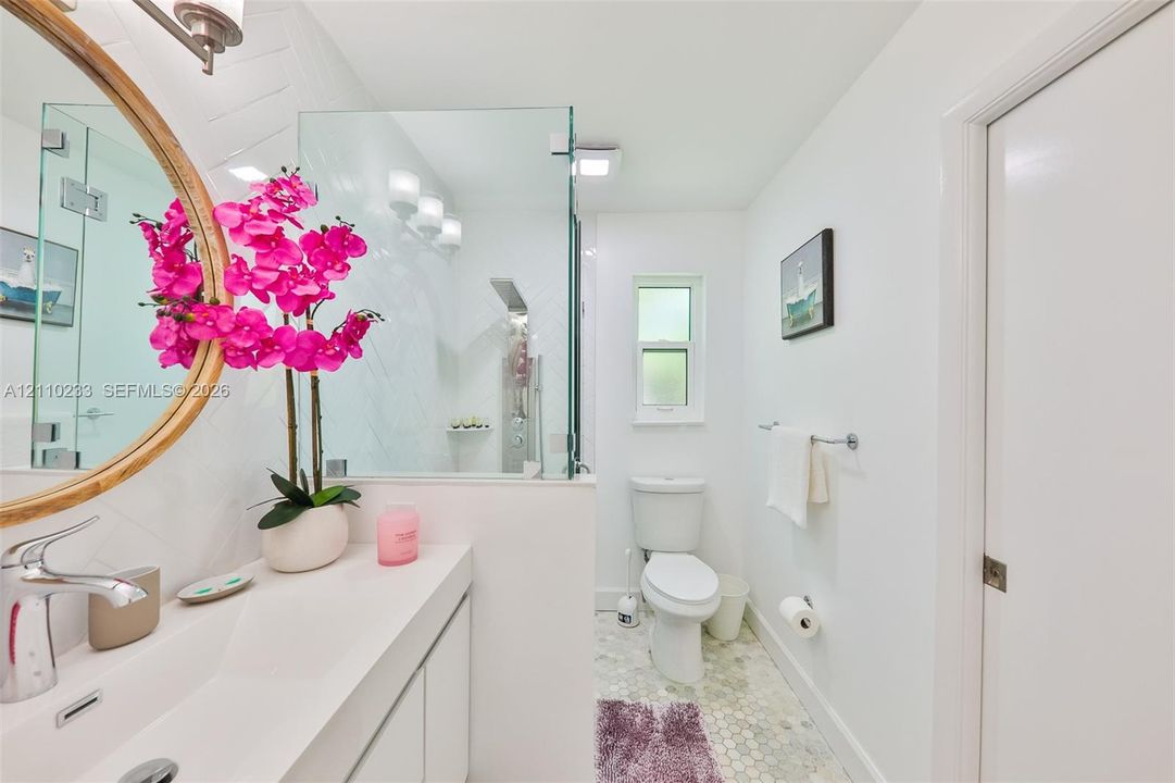 Bathroom featuring a vanity with an integrated basin, a walk-in shower with a glass enclosure and herringbone tile surround, a polished metal rainfall showerhead, and hexagonal floor tiling