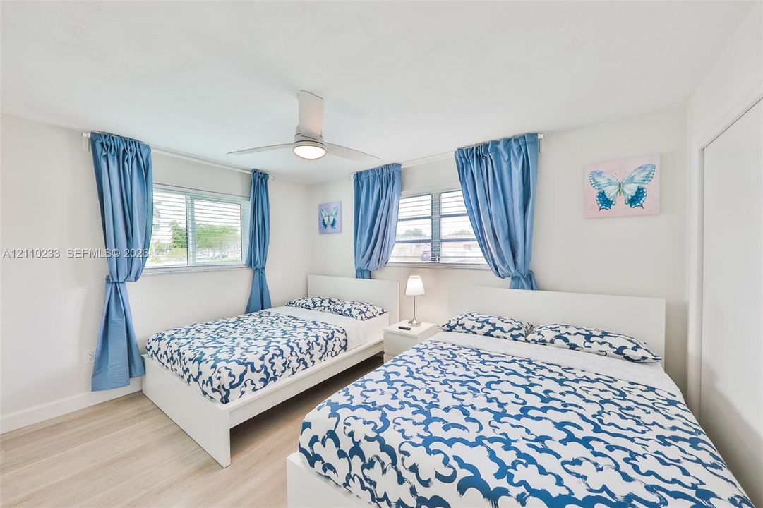 Bedroom featuring wood-finish flooring, dual horizontal sliding windows, and a central ceiling fan with integrated lighting