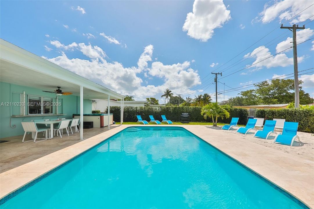 In-ground swimming pool featuring a concrete paver deck, covered outdoor patio, and perimeter hedge landscaping