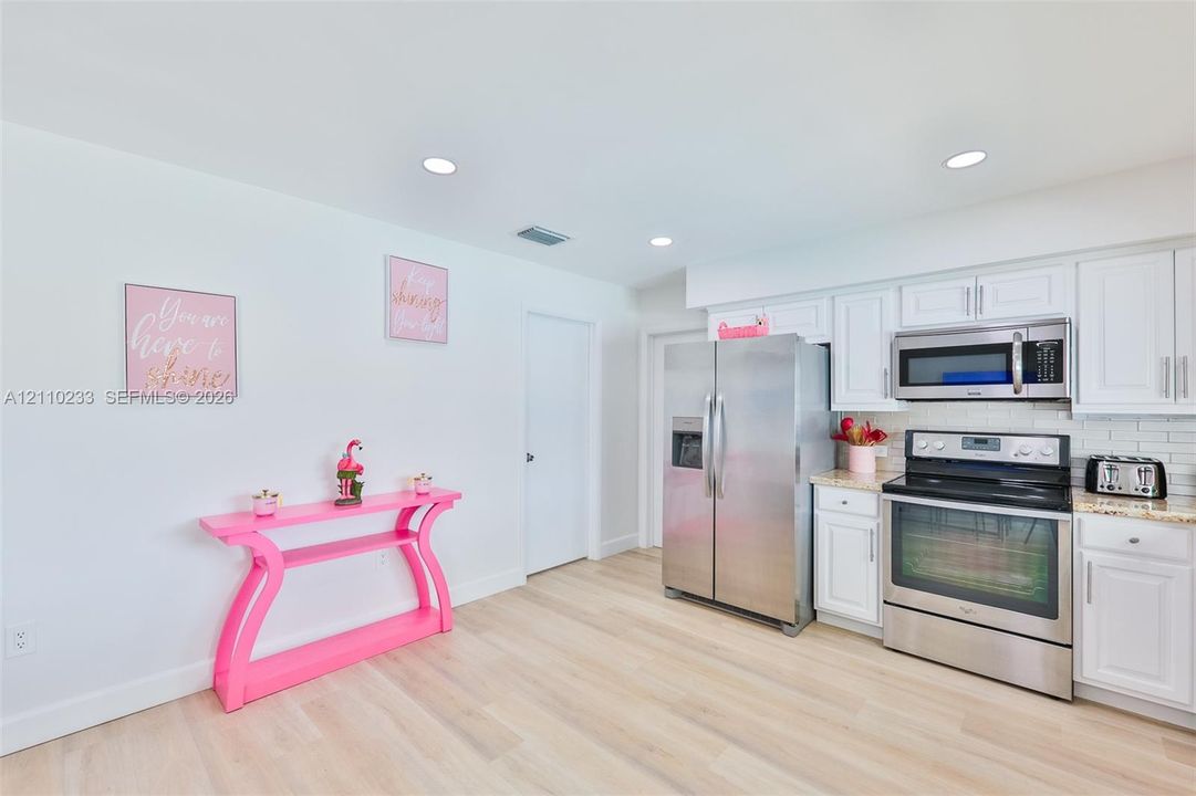 Kitchen featuring white shaker-style cabinetry, stainless steel appliances, neutral stone-finish countertops, recessed lighting, and light-toned wood-finish flooring
