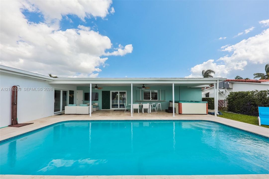 Swimming pool with stone paver decking, covered patio with dual ceiling fans, exterior wall-mounted shower fixture, and built-in hot tub