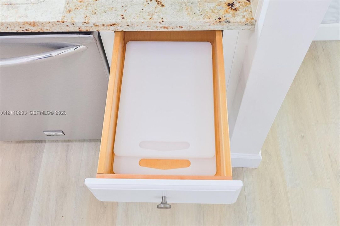 Custom-fit drawer with natural wood finish, stone-surface countertop, stainless steel dishwasher, and satin-finish metal hardware