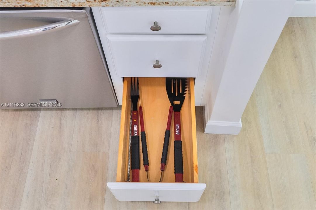 White cabinetry featuring a pull-out drawer, stainless steel dishwasher, stone-surface countertop, and wood-finish flooring
