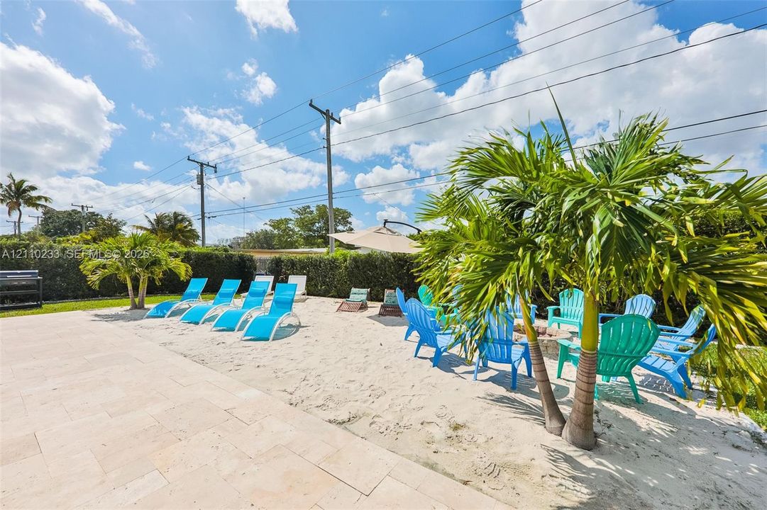Outdoor living area featuring a light-toned stone paved patio, integrated sand-filled recreational space, and mature palm trees