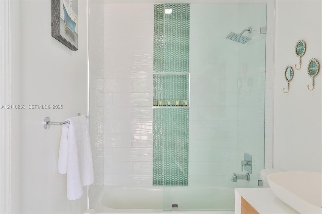 Shower and tub combination featuring white wall tiling, a vertical mosaic accent stripe, built-in recessed shelving, a glass shower panel, and a rectangular rainfall showerhead