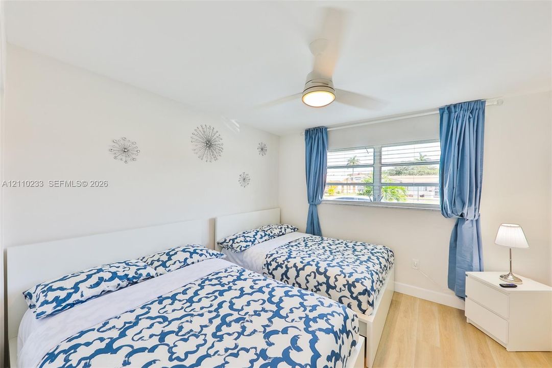 Room featuring wood-finish flooring, a ceiling-mounted light fixture with fan, and louvered windows