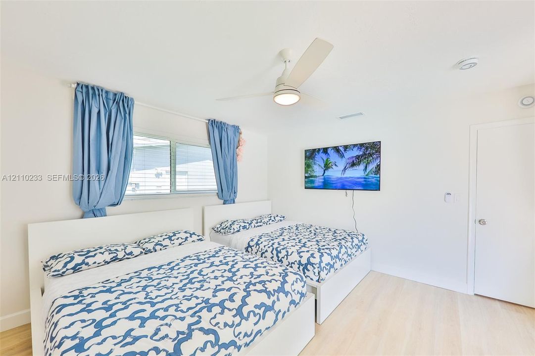 Neutral-toned room featuring wood-finish flooring, a white three-blade ceiling fan with integrated lighting, and a horizontal sliding window