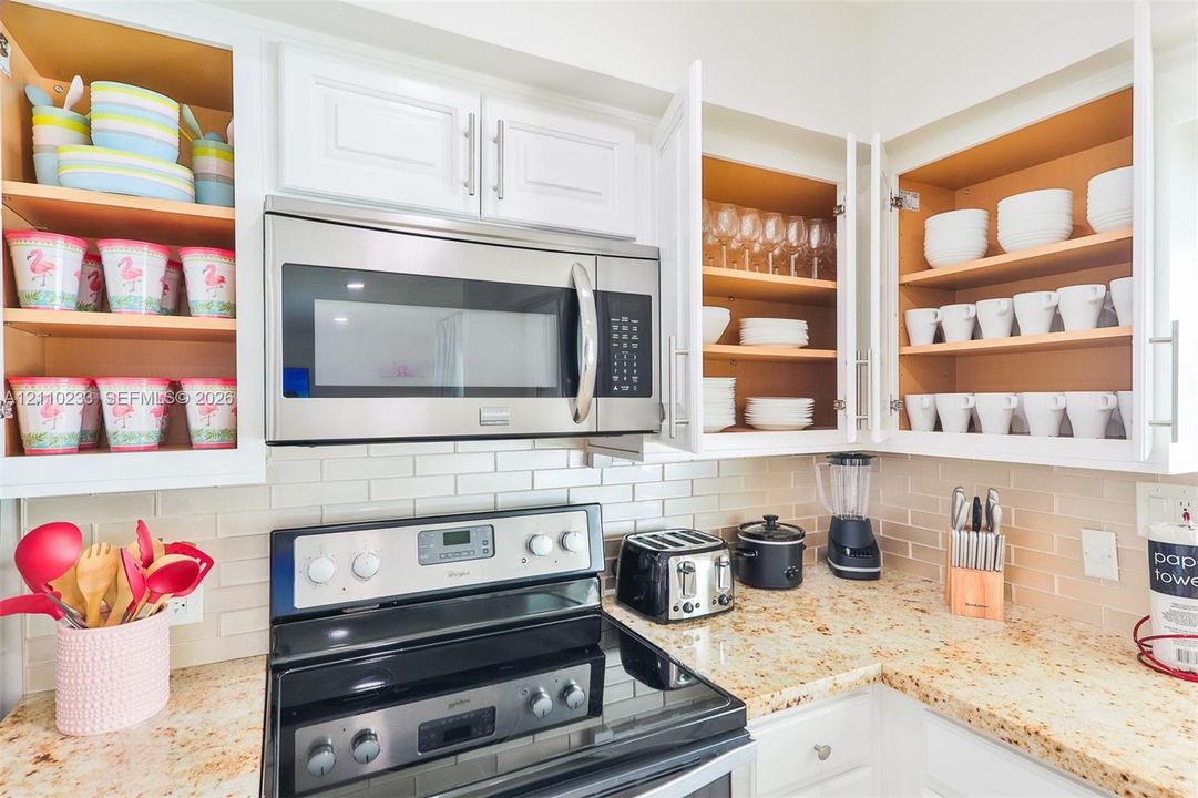 Kitchen featuring white shaker-style cabinetry, stone countertops, stainless steel microwave, stainless steel range, and a subway tile backsplash