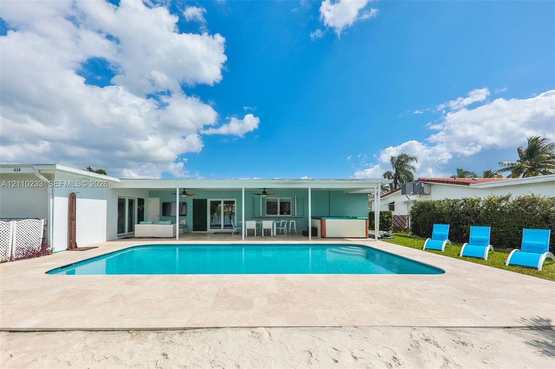 Rectangular in-ground swimming pool featuring a light-toned stone pool deck, covered outdoor patio, built-in hot tub, and exterior ceiling fans