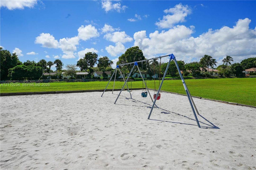 Outdoor recreation area featuring a sand-surfaced ground, metal swing set, and an expansive grass lawn