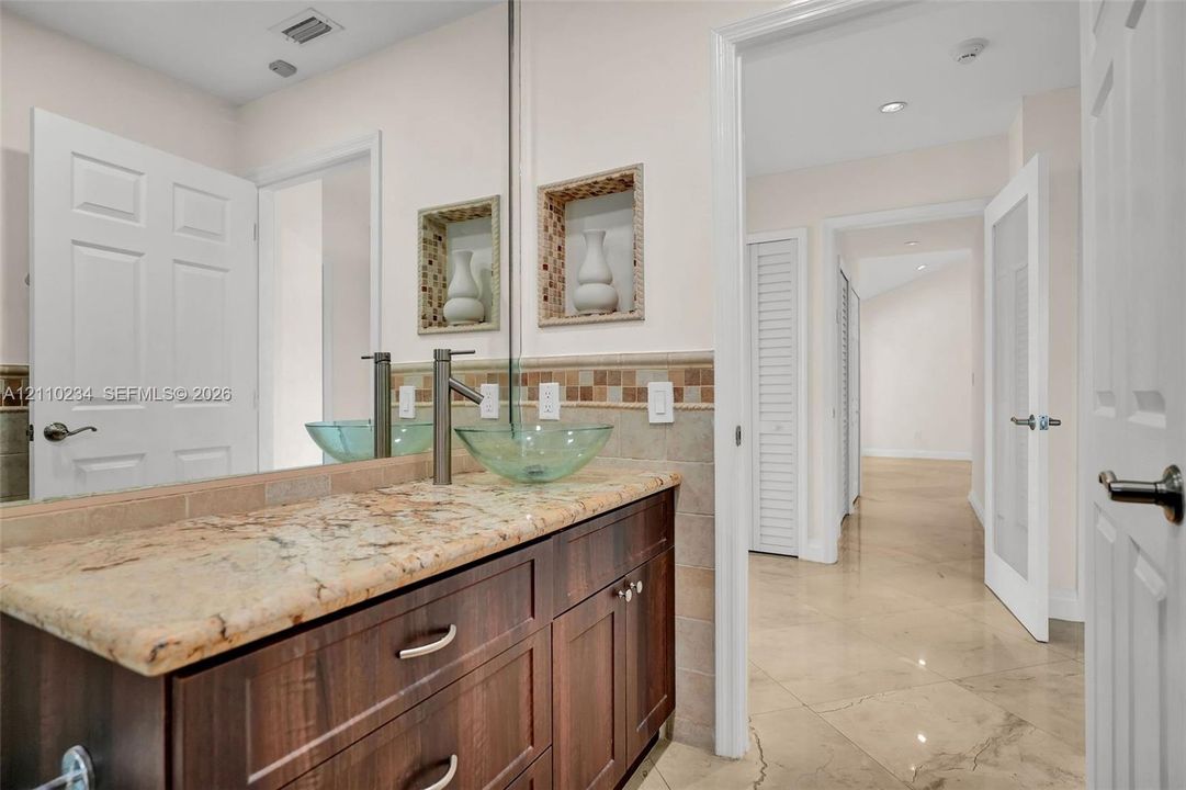 Dark wood-finish cabinetry featuring a stone-look countertop, integrated glass vessel sink, nickel-finish faucet, and built-in wall niches
