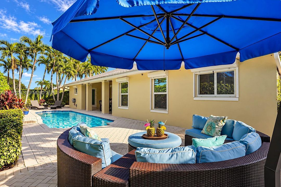 Outdoor living area featuring a paved brick patio, a built-in swimming pool, and tropical landscaping