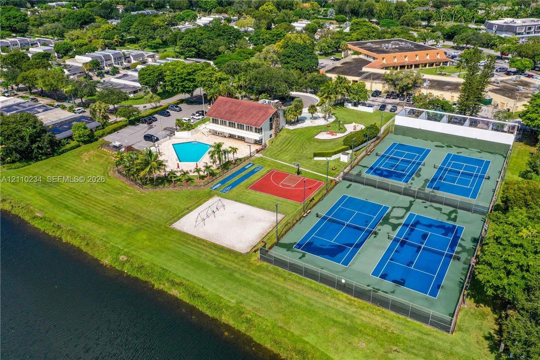 Recreational complex featuring two fenced tennis courts, a basketball court, an outdoor swimming pool, and a sand playground area