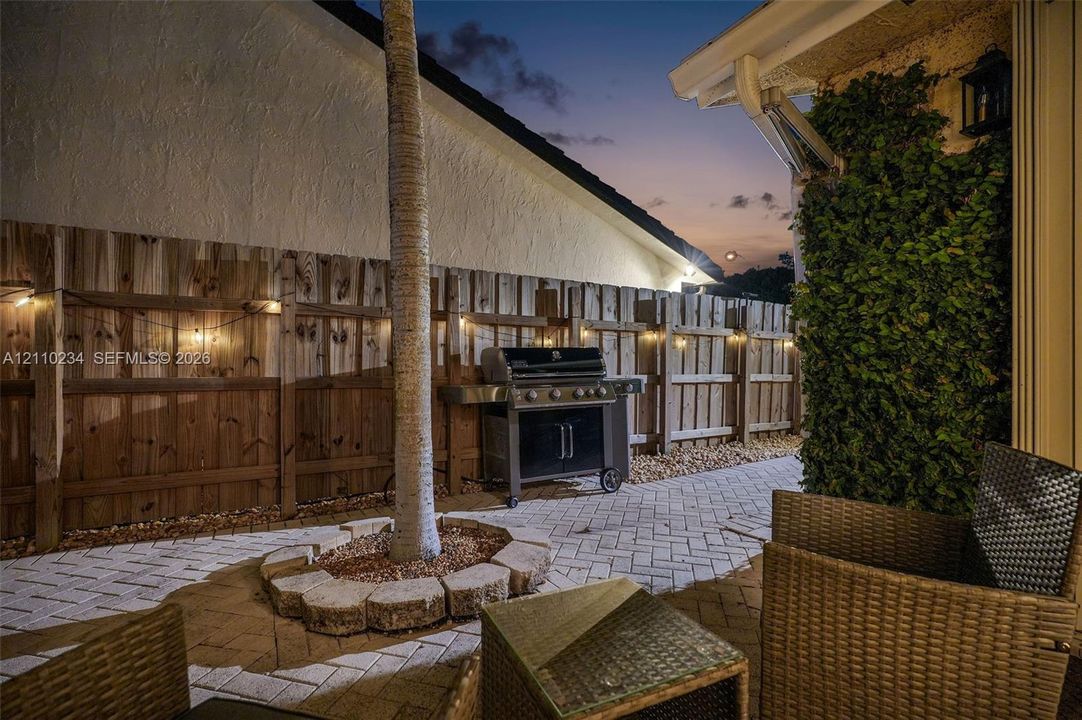 Paved patio featuring herringbone brickwork, stone-bordered landscaping, wood fencing, and wall-mounted exterior lighting