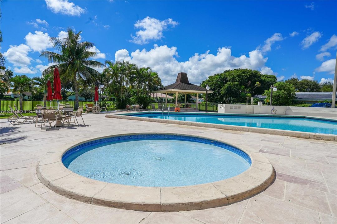 In-ground circular spa and rectangular swimming pool featuring stone-tile decking, covered gazebo, and perimeter fencing