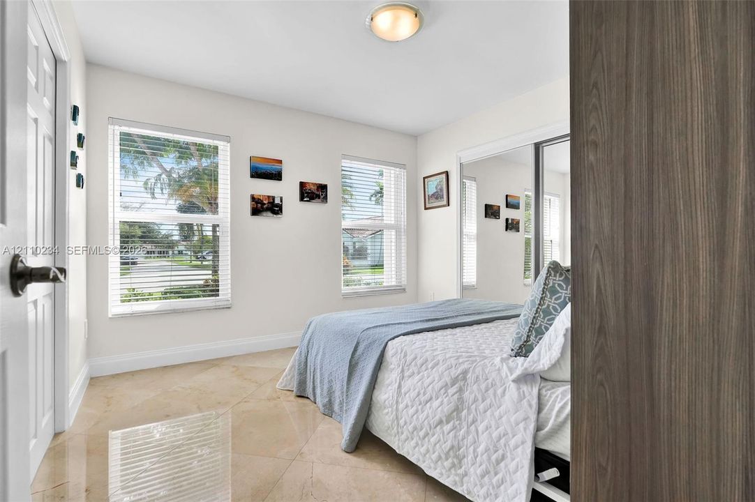 Neutral-toned tile flooring, dual windows, flush-mount ceiling light, and floor-to-ceiling mirrored closet doors