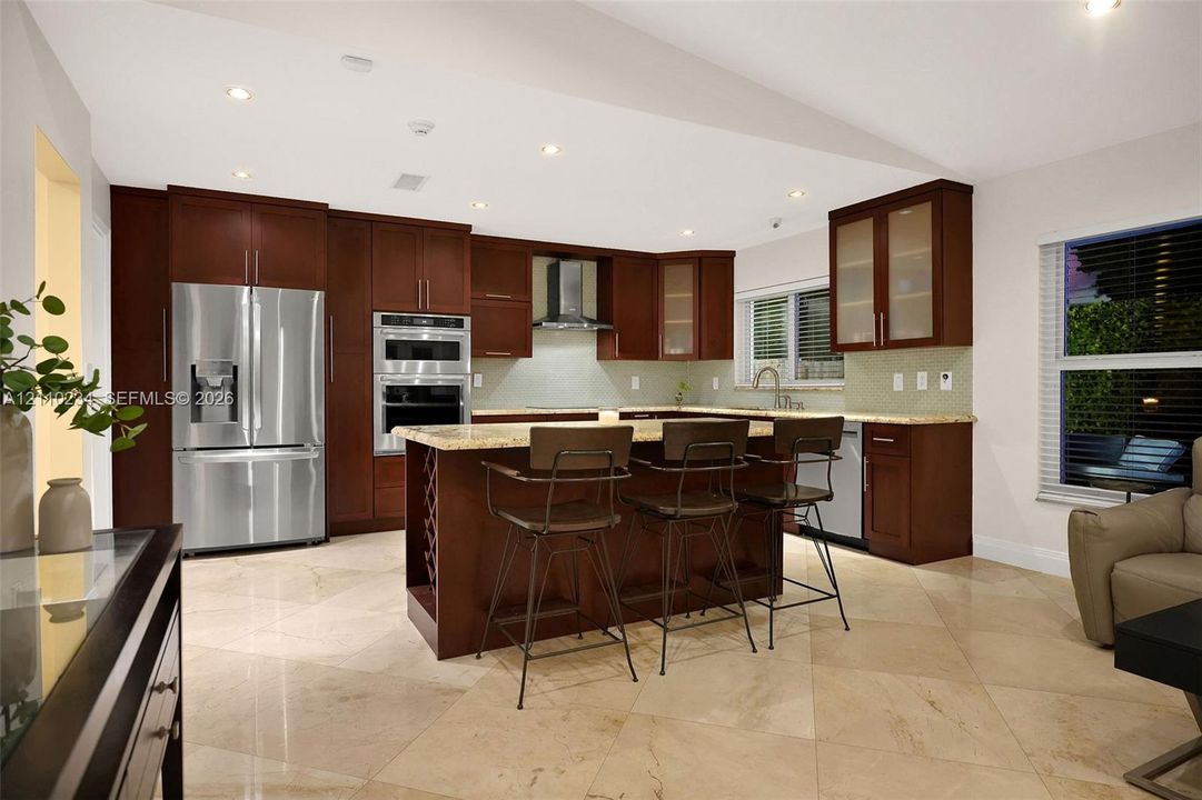 Kitchen featuring dark wood cabinetry, stainless steel appliances, built-in double wall ovens, a stone-surface center island, and tile flooring