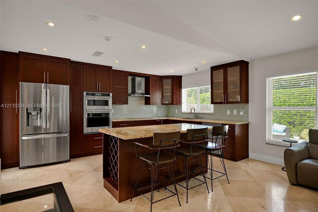 Kitchen featuring dark wood cabinetry, stainless steel appliances, stone countertops, integrated wine storage, and stone-finish flooring