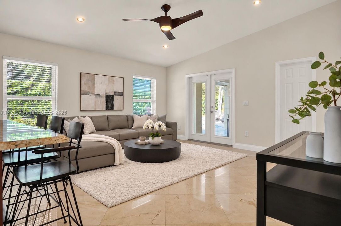 High-ceilinged living area featuring stone-finish flooring, a contemporary three-blade ceiling fan, recessed lighting, and glass-paneled double doors