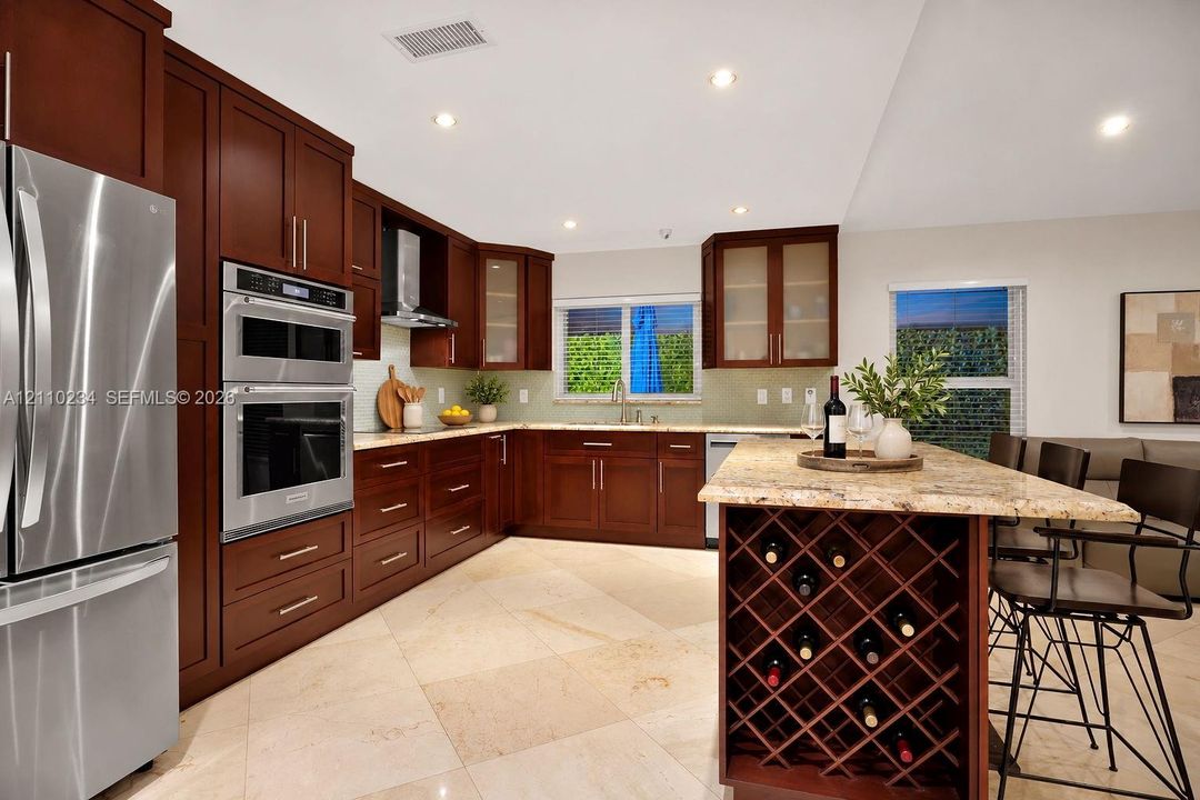 Kitchen featuring dark wood cabinetry, stainless steel double wall ovens, stone countertops, integrated wine storage, and neutral-tone tile flooring