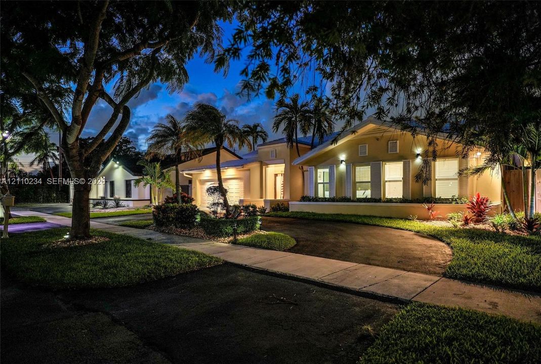 Single-story residence featuring a stucco exterior, multi-pitched roofline, paved driveway, integrated garage, and mature landscaping