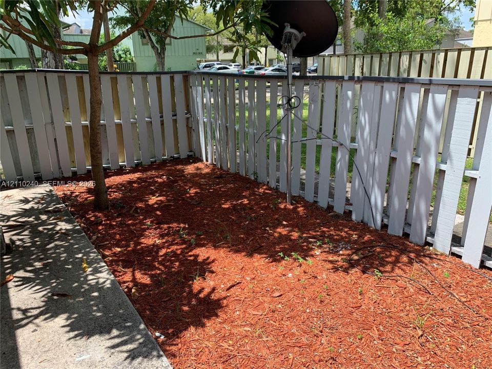Enclosed outdoor area featuring a wood-panel fence, concrete patio, mulch ground cover, and a mature tree