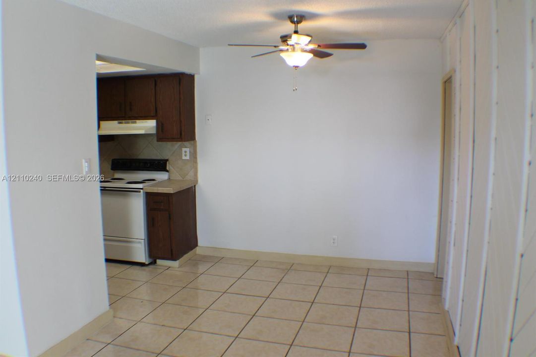 Open-concept area featuring tile flooring, ceiling fan with light fixture, and kitchen cabinetry with tiled backsplash