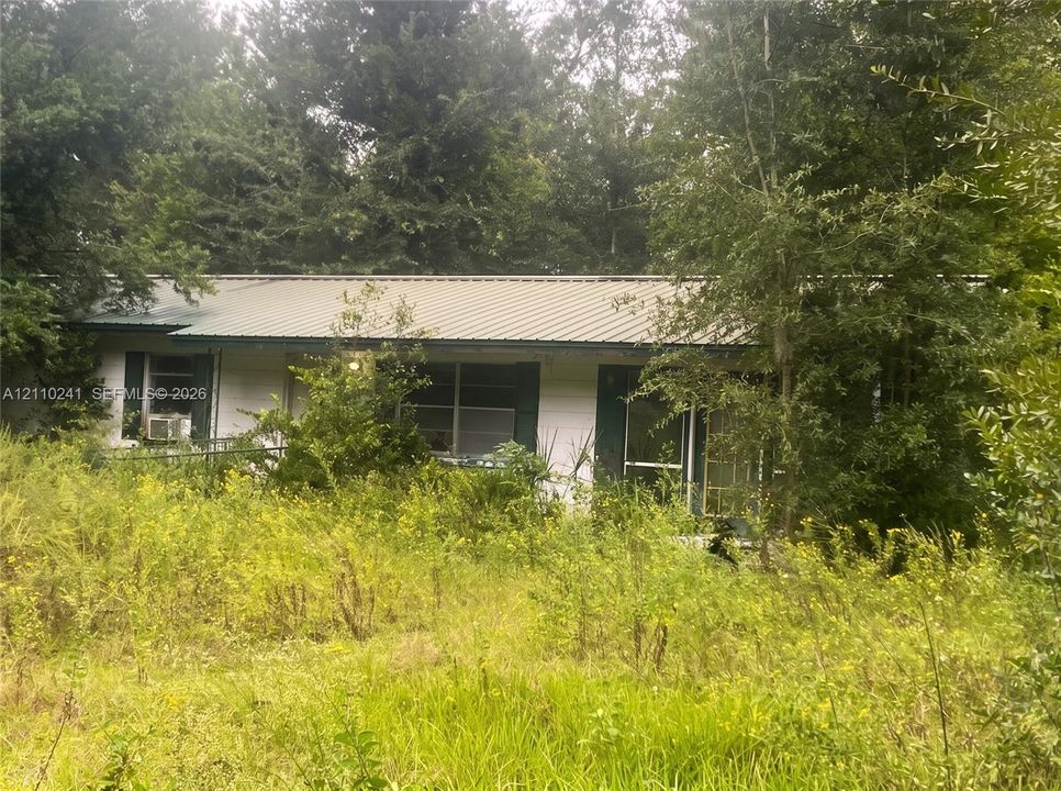 Single-story exterior featuring a metal roof, white siding, and dark shutters