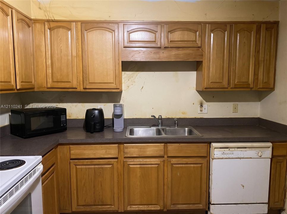 Kitchen featuring wood cabinetry, solid-surface countertops, dual-basin stainless steel sink with metal faucet, and built-in dishwasher