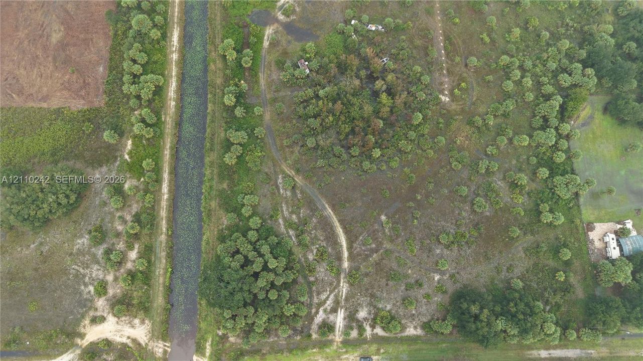 Aerial perspective of a sprawling parcel featuring native vegetation, clusters of mature trees, natural terrain, and an irrigation canal