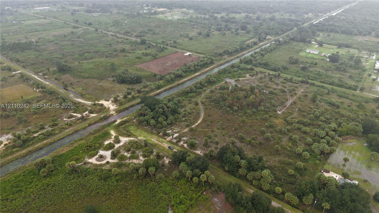Expansive acreage featuring natural vegetation, native palms, cleared paths, and a bordering canal