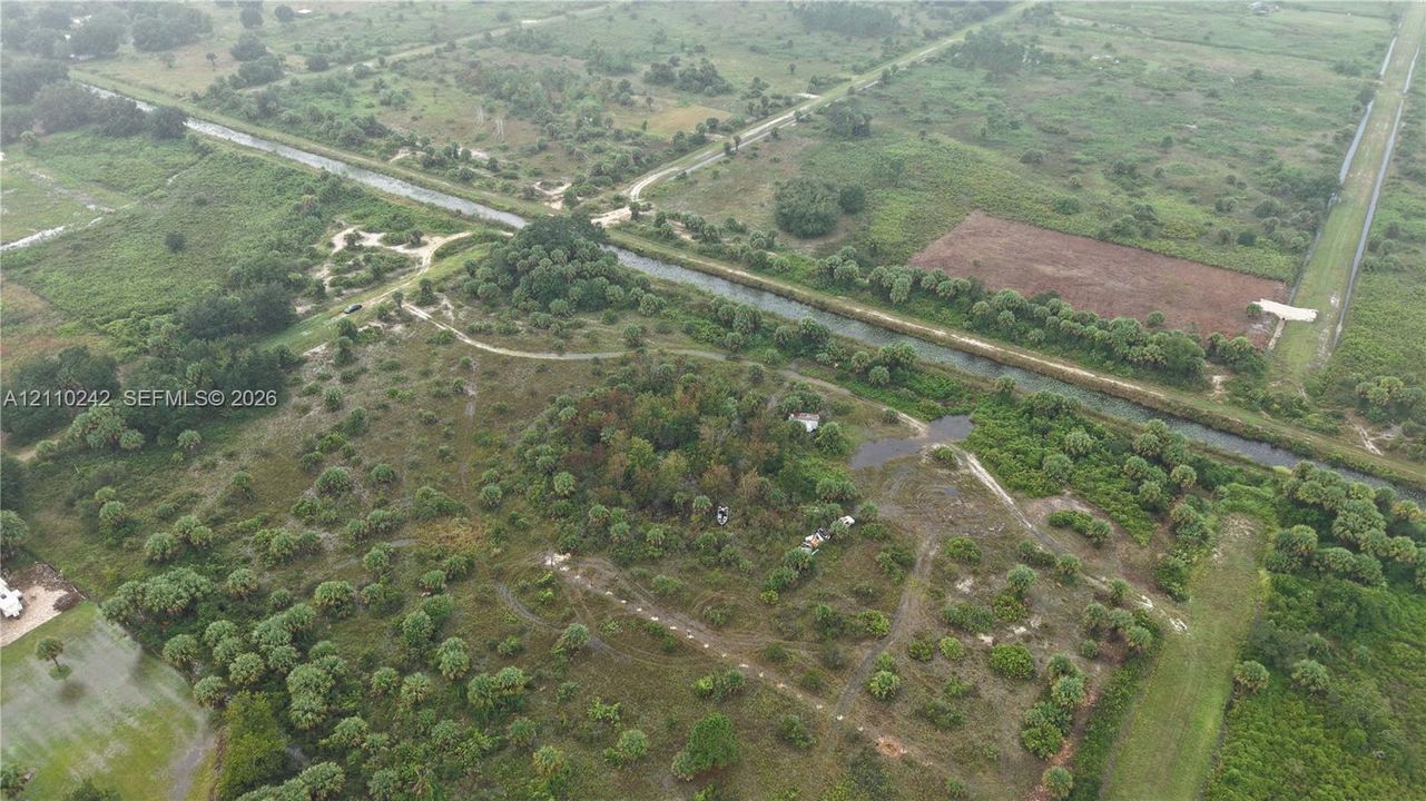 Aerial perspective of expansive acreage featuring native vegetation, scattered mature trees, and direct frontage along a canal