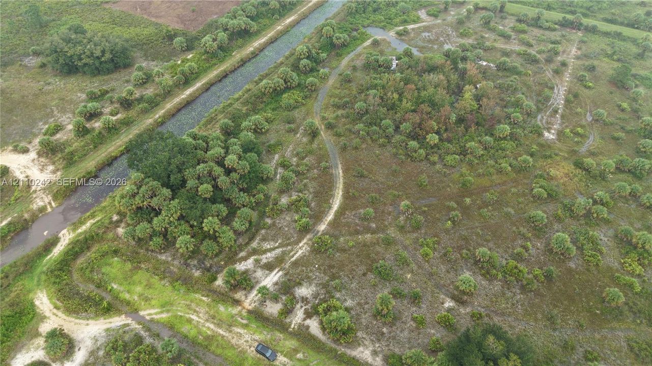 Expansive acreage featuring native vegetation, clusters of mature trees, dirt trails, and direct frontage on a water canal