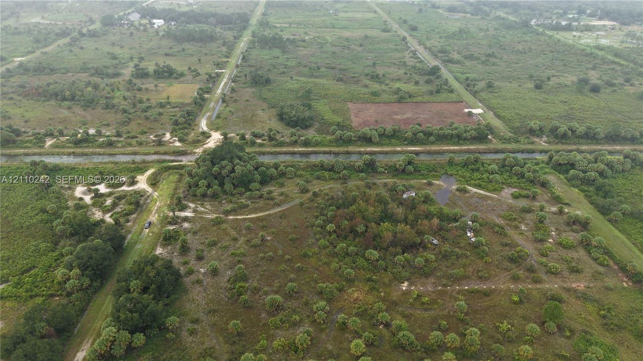 Expansive acreage featuring natural vegetation, native tree clusters, unpaved terrain, and a bordering canal