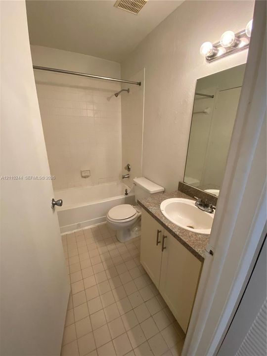Bathroom featuring a vanity with a stone-finish countertop and integrated basin, tile flooring, tub-shower combination with tile surround, and a wall-mounted light fixture