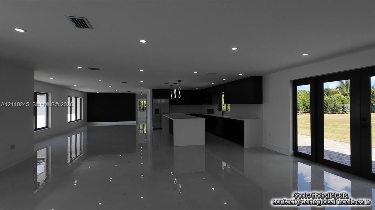 Open-concept interior featuring large-format tile flooring, recessed ceiling lighting, a central island with a quartz countertop, minimalist dark cabinetry, and glass-paneled double doors
