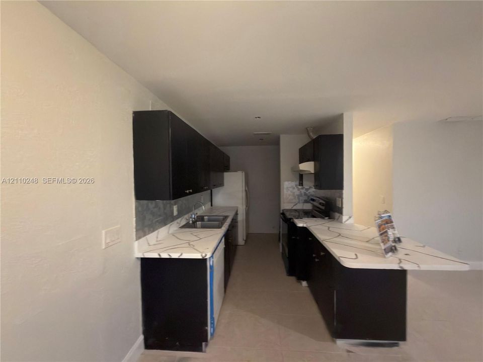 Kitchen featuring dark cabinetry, stone-patterned countertops, a dual-basin stainless steel sink, and a breakfast bar
