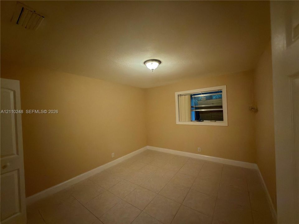 Interior room featuring neutral-toned walls, tile flooring, a central flush-mount ceiling light fixture, and an interior window