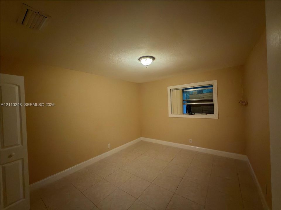 Room featuring neutral wall paint, tile flooring, a centered ceiling-mounted light fixture, and a window with white trim