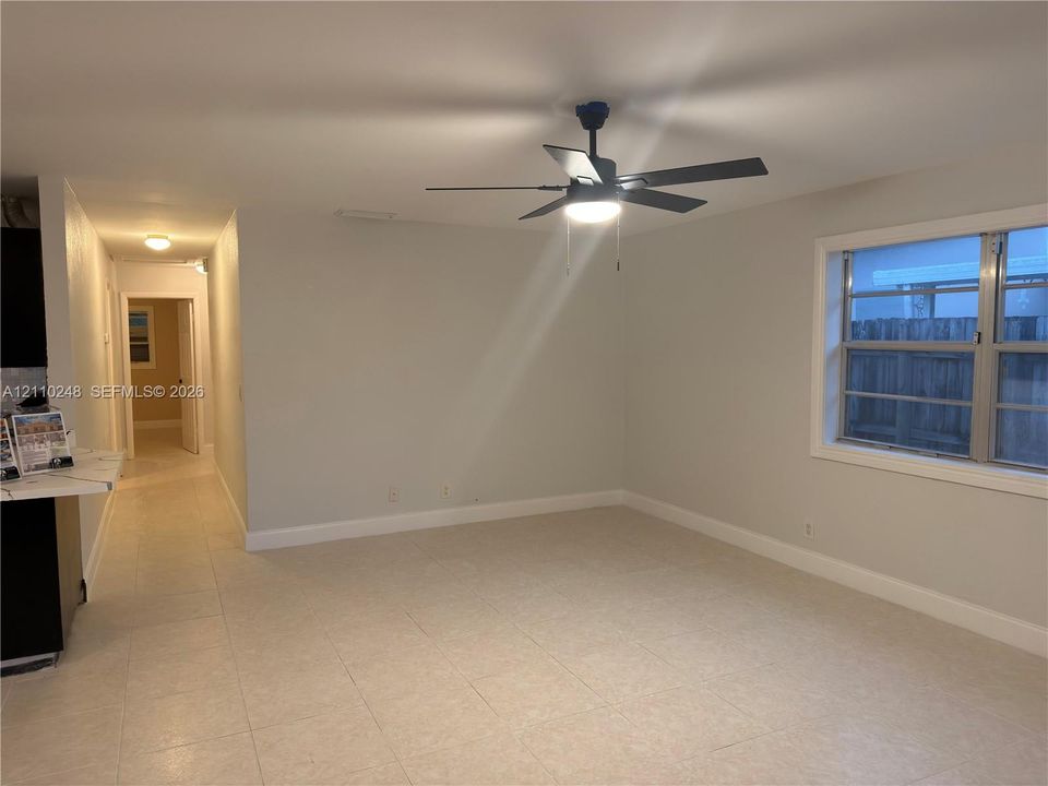 Neutral-toned interior space featuring light tile flooring, a multi-blade ceiling fan with integrated lighting, and a multi-pane window