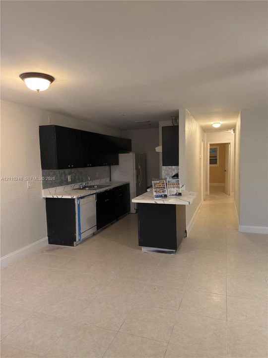 Kitchen featuring black cabinetry, light-toned countertops with patterned backsplash, a central island, and tile flooring