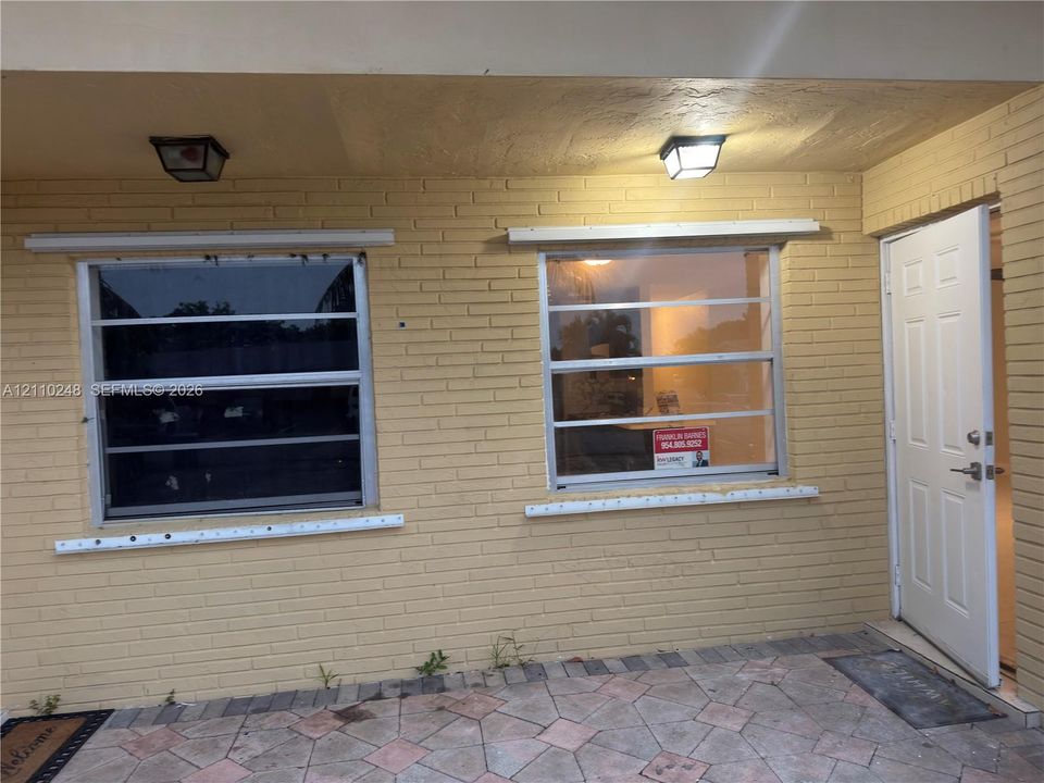 Exterior facade featuring painted brick masonry, horizontal sliding windows, and a paved stone patio