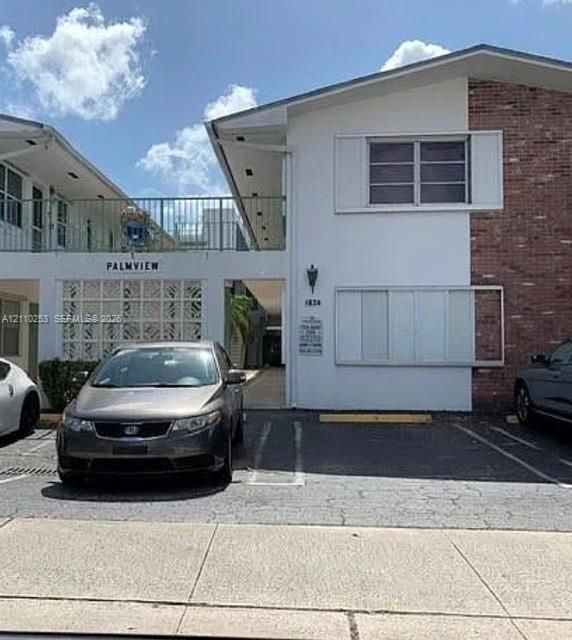 Multi-level exterior featuring white stucco finish, red brick accents, decorative breeze block wall detailing, and a metal balcony railing