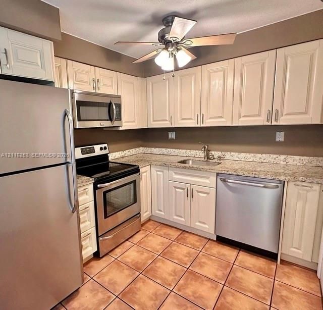 Kitchen featuring off-white cabinetry, stone-finish countertops, stainless steel appliances, a stainless steel sink with a high-arch faucet, and tile flooring