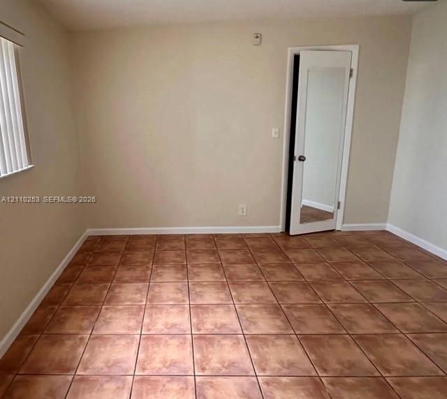 Room featuring neutral-toned walls, tile flooring, vertical window blinds, and a door with an integrated mirror panel