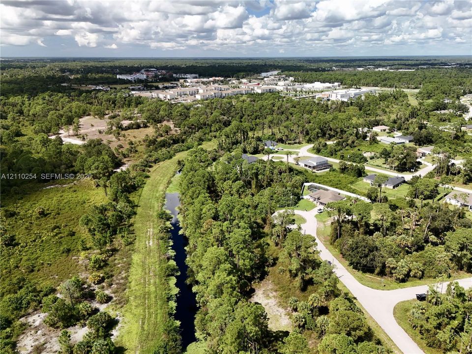 Aerial perspective featuring densely wooded landscape, natural waterway, paved roads, and residential lots