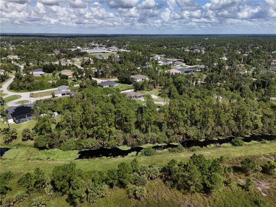 Aerial perspective of a sprawling residential locale featuring expansive green space, abundant mature trees, and a bordering waterway